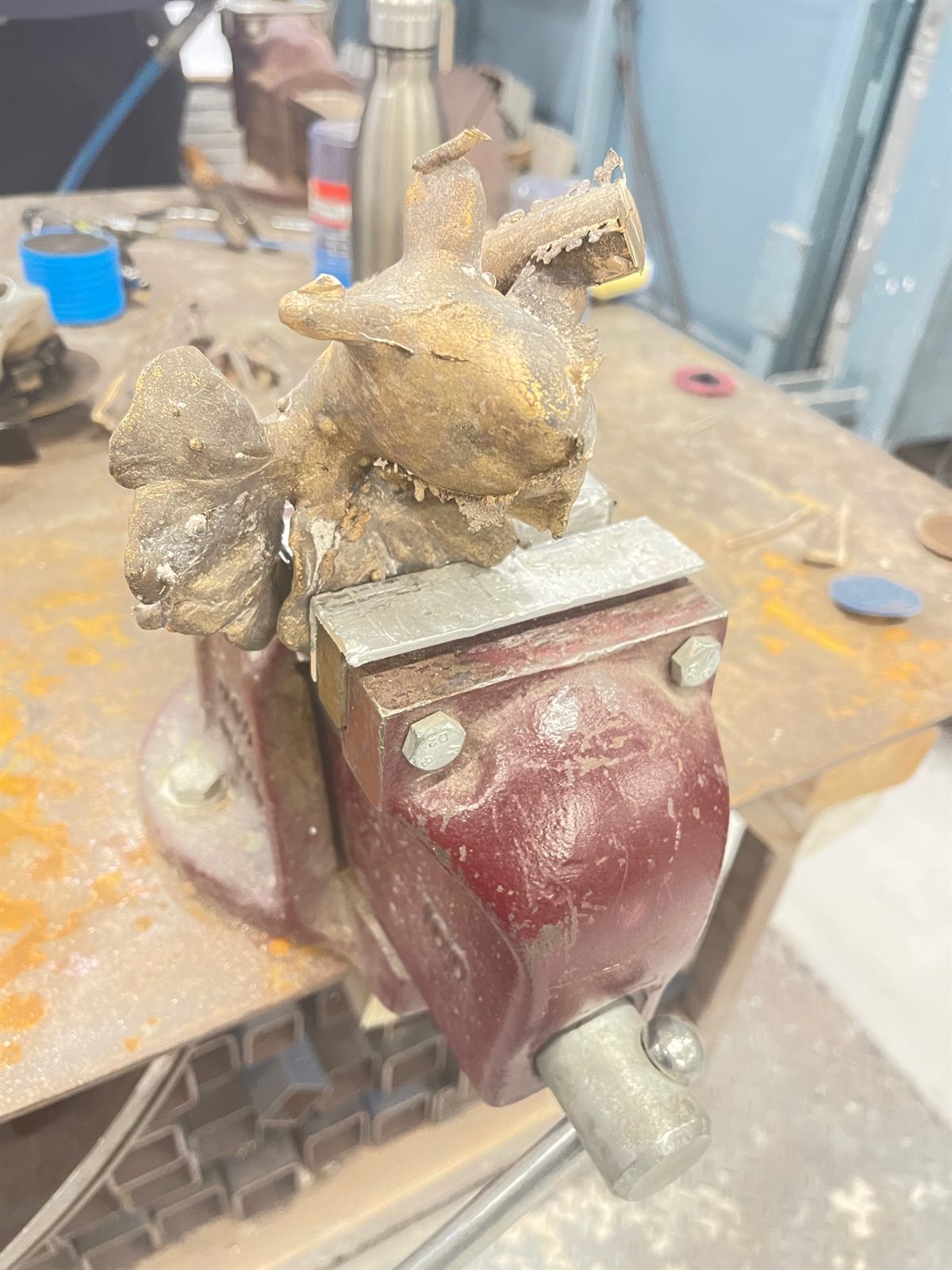 Goldfish — the raw bronze casting clamped in a vice, still covered in investment
