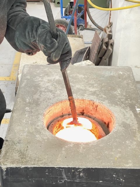 Molten bronze glowing in the furnace, being skimmed before the pour