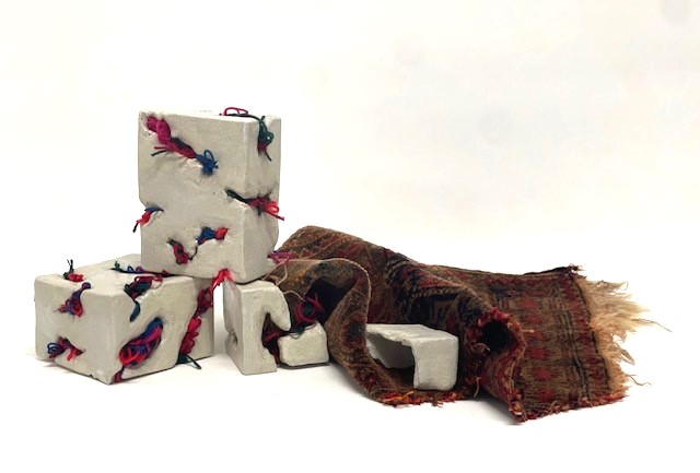 Threads of Home — an old Persian rug spread beside stacked white clay blocks threaded with red and blue wool