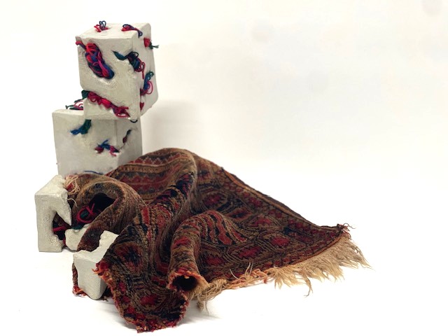 Threads of Home — the Persian rug gathered into folds beside the stacked clay blocks