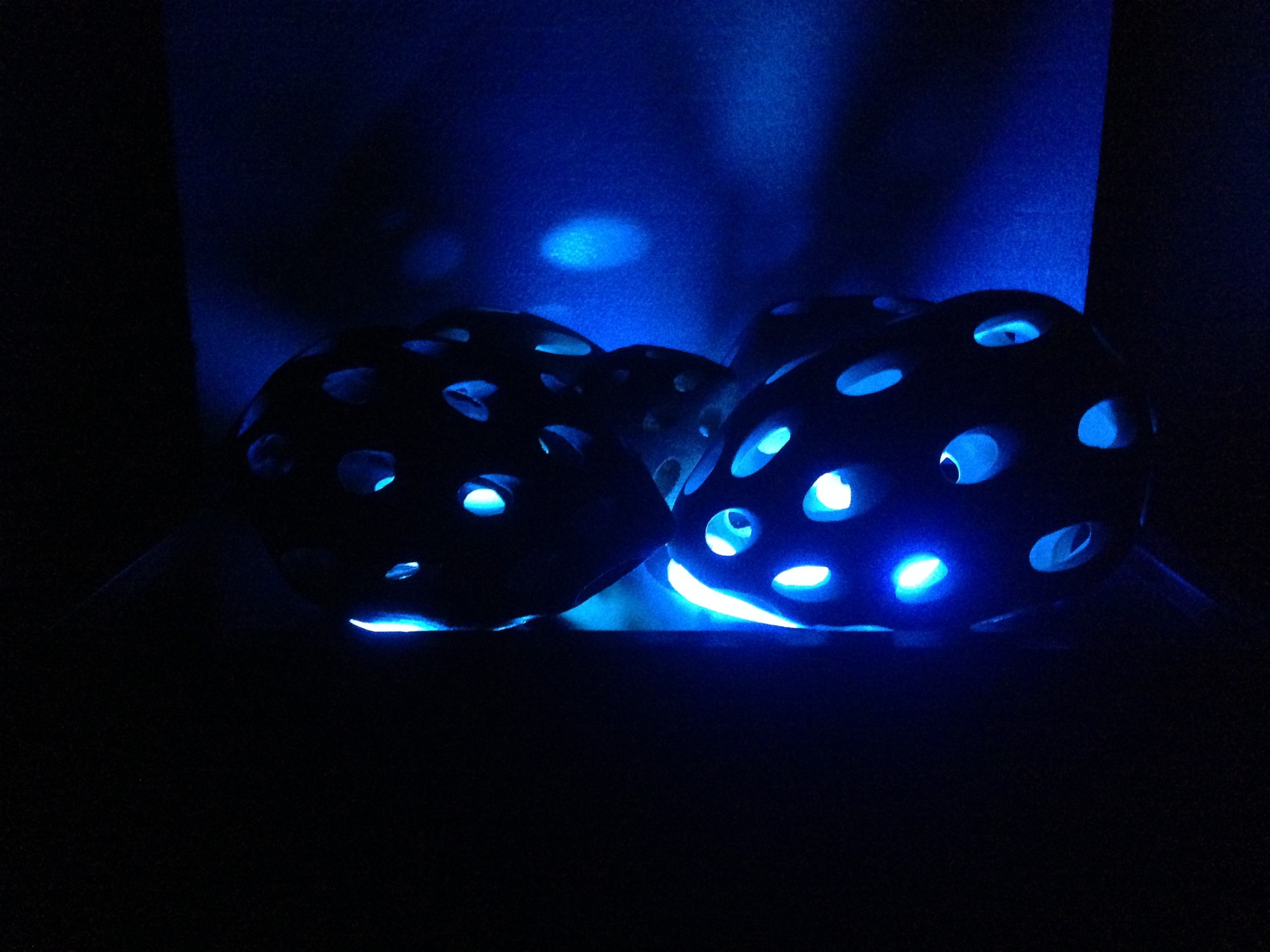 The Touch of Memory — pierced ceramic forms lit from within by blue light, their openings casting pools of light onto the wall behind